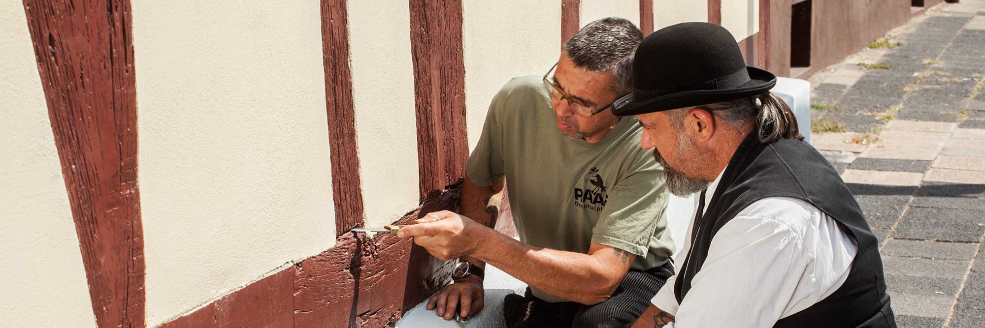 Restaurator Thorsten Raab untersucht gemeinsam mit seinem Mitarbeiter mithilfe eines Messers Schäden am Fachwerkhaus